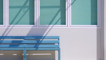 Two wooden benches in front of glass windows and blue sun blinds with sunlight and shadow on vintage white concrete house wall surface in minimal style