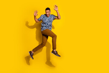 Full length photo of cheerful positive guy dressed print shirt jumping high running empty space isolated yellow color background