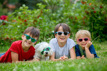 Three children and cute white puppy pet dog with sunglasses, having fun in garden