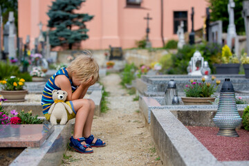 Little toddler boy, sitting on a cemetery, feeling sad