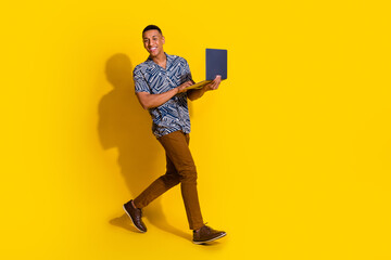 Full length photo of attractive funny guy wear print shirt texting modern gadget walking emtpy space isolated yellow color background