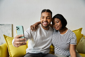 Naklejka premium An African American couple takes a selfie on a yellow couch.