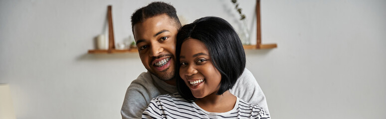 An African American couple smiles happily together in their home.