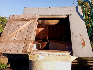 A well in the village with an open door and a bucket for collecting water. Old village well with...