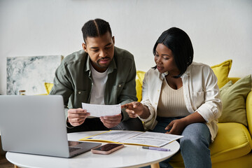A loving African American couple sits at a table in their home, looking over documents together.