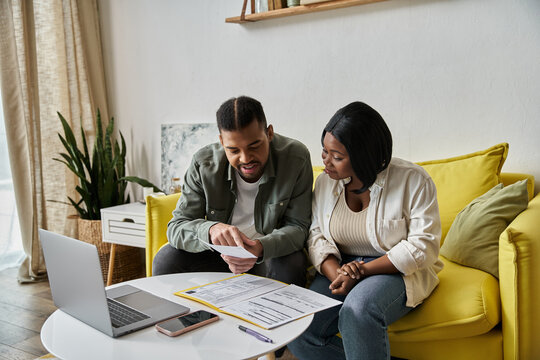 A african american couple on yellow couch reviews documents in home office. - Powered by Adobe