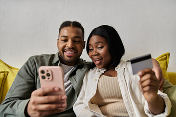 An African American couple smiles at their phone while shopping online at home.