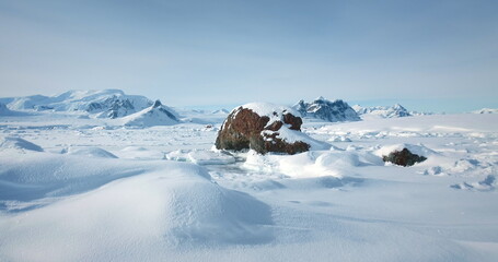 Winter Antarctic landscape in sunny day, blue sky. Desert white land of snow and ice, mountain range in background. Breathtaking travel journey over frozen Antarctica landscape. Low angle drone shot