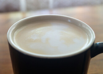 Coffee with milk in a black cup close-up. Coffee foam with milk in a cup