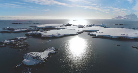 Aerial flight over ice floes floating in Arctic ocean. Untouched wilderness of Antarctica winter landscape. Rocky coastline, snow, cold water, mountains in background. Explore travel to South Pole