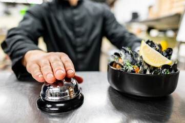 Chef in a kitchen ringing a service bell beside a bowl of mussels with lemon