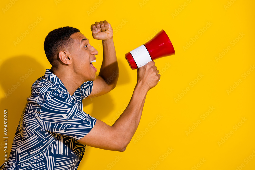 Poster Photo of handsome lucky guy wear print shirt screaming loud speaker emtpy space isolated yellow color background