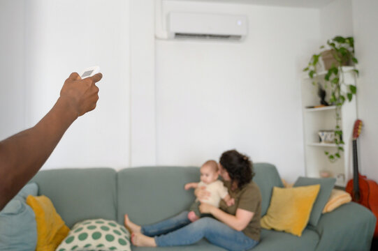 Man adjusting air conditioner while mother cuddles baby