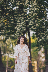 Beautiful young in light romantic dress. Portrait of young woman near blooming tree in a European city. Spring. Beautiful woman with long hair in Spring blossom garden.