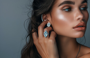 A beautiful woman wearing an aquamarine ring and earrings with diamonds, touching her ear to show the details of jewelry