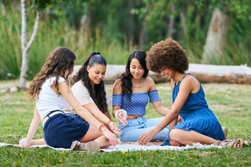 Four women are sitting on a blanket in a park, playing a game