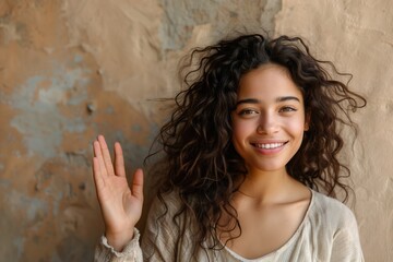 Naklejka premium Smiling Woman with Curly Hair Waving Against Textured Wall 