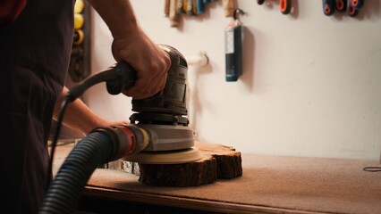 Carpenter using angle grinder on timber block to smooth surfaces with sandpaper. Woodworking professional using orbital sander equipment for furniture assembling job in studio, close up, camera B