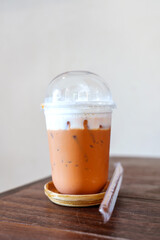 Iced Thai milk tea in a clear plastic glass on the wooden table in a cafe bakery.