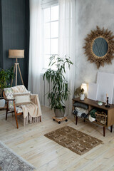 Stylish corner features a colorful armchair, soft blanket, and decorative pillow. Wooden floor lamp, potted plants, and a sunburst mirror on the wall. White curtains filter natural light