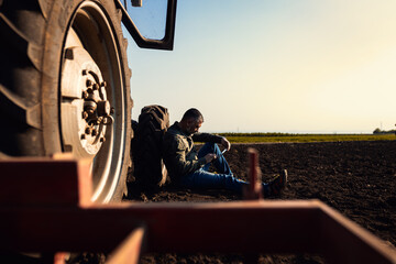 Farmer siting and using tablet while resting after cultivation of soil leaning on tractor tire. © Zoran Zeremski