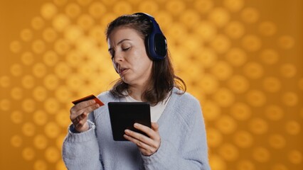 Woman buying electronic books for ereader using credit card, isolated over studio background. Bookworm listening music in headphones, purchasing ebooks, typing on tablet screen, camera B