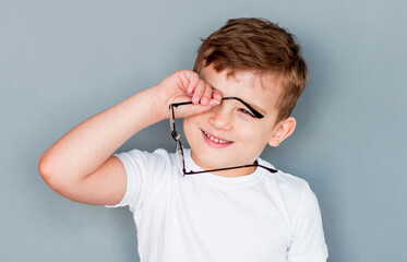 Small school guy rubs his eyes standing on gray background. Dry eyes, pain. Bad eyesight, fatigue