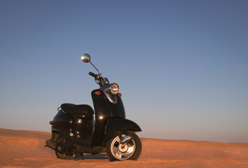 The Retro black scooter at sunset in the golden sand of the Namib Desert