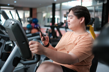 Overweight man using elliptical while texting