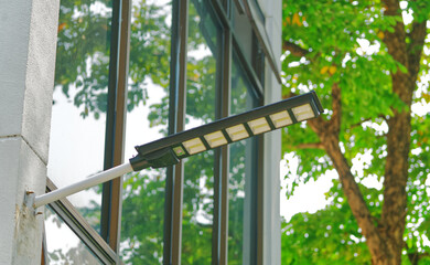 Solar cell lamp on the wall of a mirror building with the background of a part of the big tree, mirror with reflection from trees.