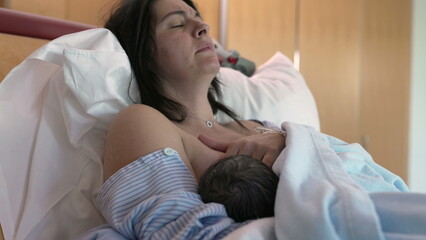 New mother struggles with breastfeeding pain after giving birth to baby seated at hospital bed,...