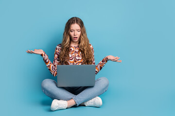 Full size photo of nice young girl sit floor laptop shrug shoulders wear top isolated on blue color...