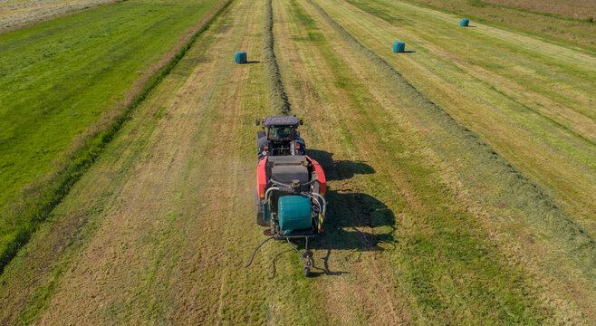 Schwarzer Treker oder Traktor mit einer roten Stroh Festkammerpresse bei der Strohernte auf einem gem&auml;hten Feld