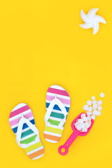 Summer seaside vacation travel concept with rainbow flip flops, decorative seashells, abstract starfish sun on yellow background. Holiday fun with LGBT theme.