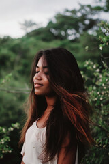 Naklejka premium Portrait of a young girl with dark hair against a background of trees, the girl stands in greenery, natural photo