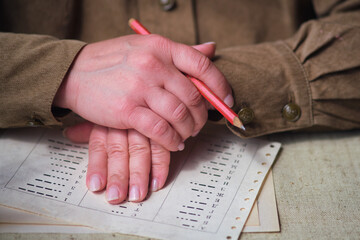 The hands of a soldier in a USSR uniform from the Second World War over a document with Morse code. Historical items from the times of the Soviet Union