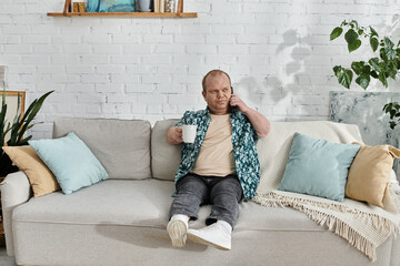 Obraz premium A man with inclusivity sits on a couch, holding a cup of coffee and talking on the phone.