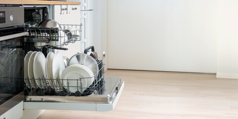 Open built-in dishwasher machine with clean cutlery, dishes, plates in white modern kitchen. Side view banner