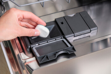 Dishwasher tablets, woman puts the capsule in the dishwashing machine before washing tableware and...