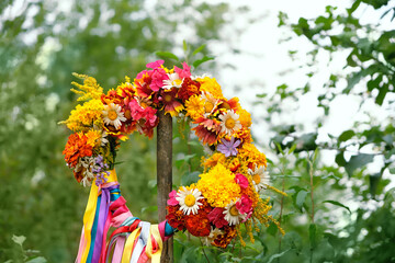 flowers wreath with colorful ribbons on wooden post on meadow. summer background. Floral crown,...