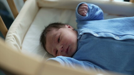 Newborn baby lying in a crib, dressed in blue, looking around with curiosity. early life, innocence, and the cozy environment of a nursery. Ideal for themes of parenthood and newborn care