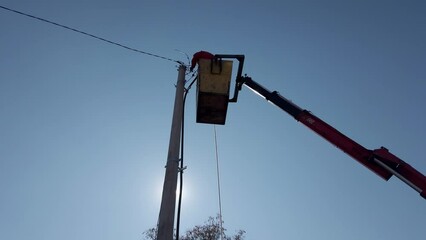 Utility worker repairing electric line post with crane. A utility worker uses a crane for high elevation work, repairing an electric line post under a clear blue sky