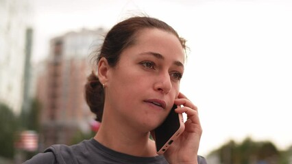 Young woman talking on smartphone on street in city outdoor. Girl with cell phone chatting with friends. Smiling person making answering call by cellphone. Woman having conversation by mobile