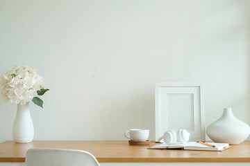 Empty picture frame, coffee cup, headphone and ceramic vase on wooden table.