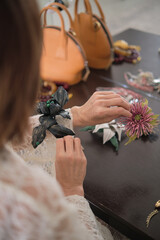 A close-up of a woman arranging floral brooches on a table, emphasizing her careful consideration....