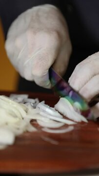 Close up view of male hands chopping  onion on wooden cutting board with knife