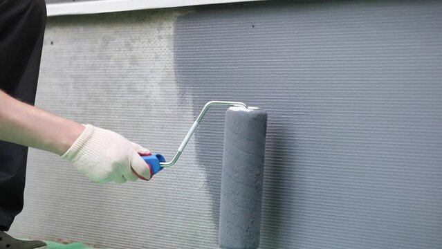 Man applying grey paint with roller brush on the wall, closeup video