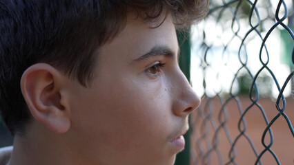 Close-Up Portrait of a Teen Boy by a Chain Link Fence, Reflecting Deep Thought and Concentration