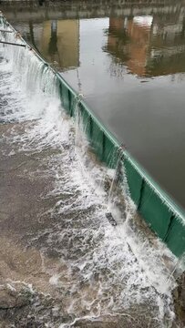 Vertical view of turbulent water cascading over a green rubber dam, reflecting the technology and industry behind irrigation and water management control systems.
