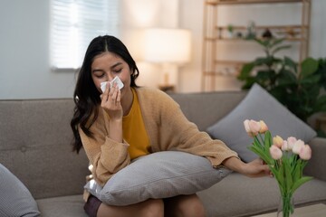 Woman sneezing due to pollen allergy at home. Concept of seasonal allergies